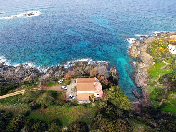 An aerial view of a coastal property with a house, a driveway, and a small parking area.