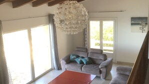 Un salon spacieux avec un plafond en bois, un grand lustre, un canapé gris et une table basse rouge.