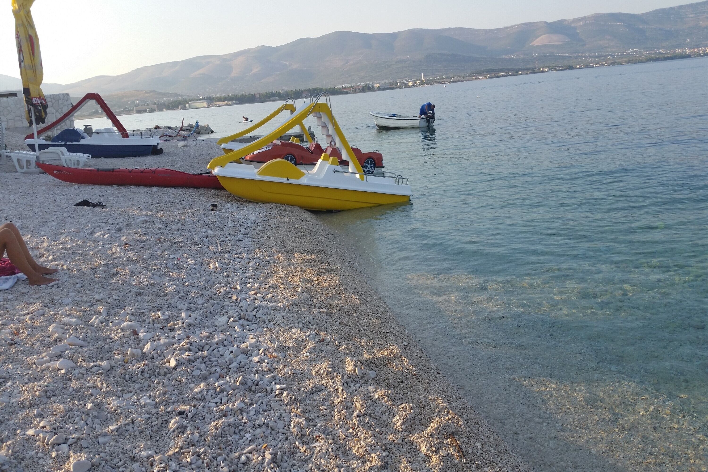 A pebbled beach with several paddle boats and a person sitting on the sand.