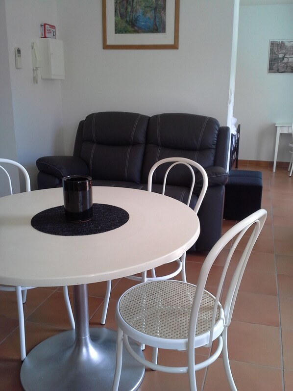 A dining area with a round table, white chairs, and a black coffee pot.
