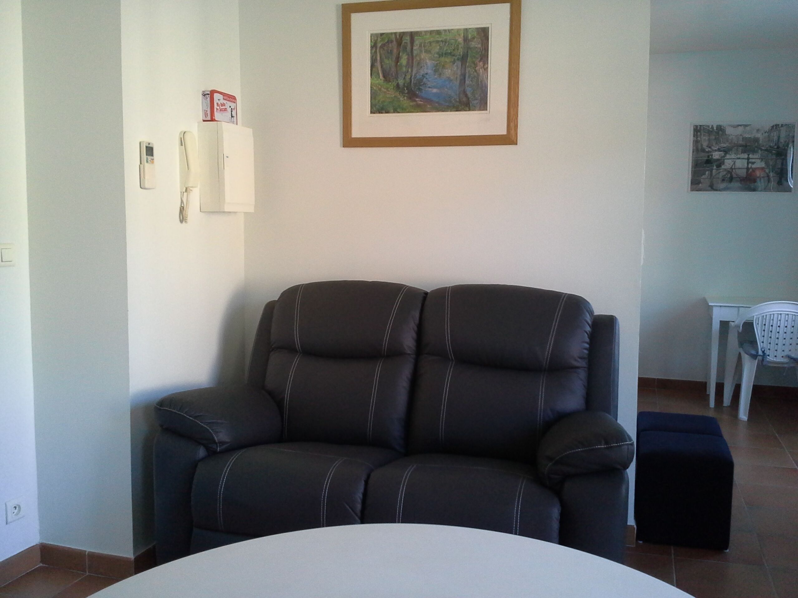 A living room with a dark leather sofa, a white round table, and a framed painting on the wall.