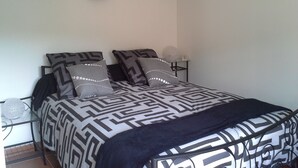 Ein Schlafzimmer mit einem Bett, das eine geometrische Tagesdecke, zwei passend gestaltete Kissen, eine schwarze Tagesdecke und einen kleinen Nachttisch mit einer Lampe zeigt.