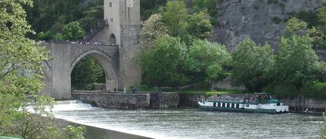 A stone bridge with a tower, a boat on the river, and greenery around.
