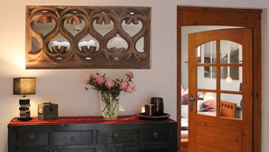Une pièce avec une porte en bois, une commode à tiroirs, un vase avec des fleurs, une lampe et un élément décoratif mural.