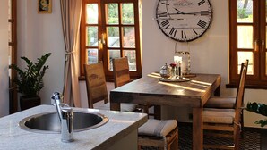 Un coin repas avec une table en bois, des chaises, une grande horloge murale et une fenêtre avec des rideaux.