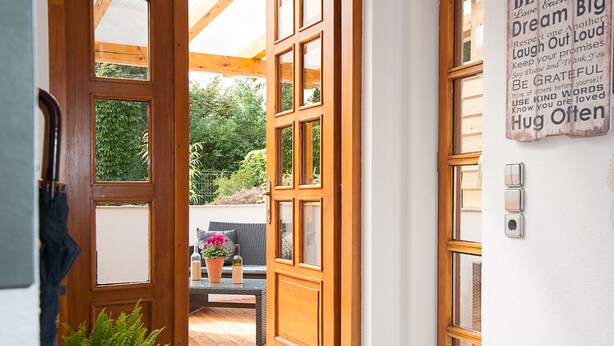 Une porte en bois donnant sur un patio extérieur, où se trouvent un banc et des plantes en pot.