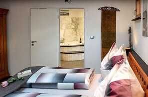 Een slaapkamer met een bed, een houten hoofdbord, een deur naar een badkamer en een klein tafeltje met een bloem.