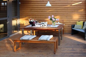 An outdoor wooden deck with a table set for a meal, a bench, and a sofa.