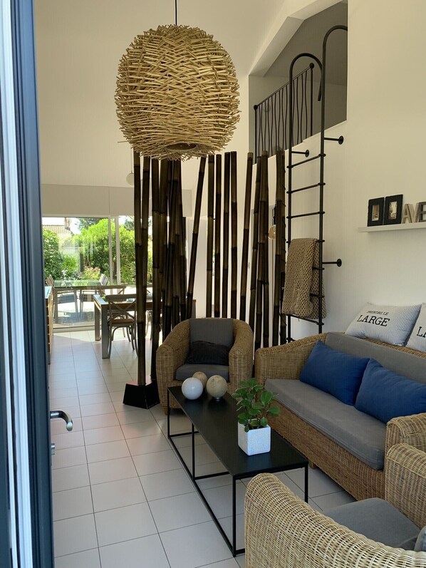 A modern living room with wicker furniture, a black coffee table, and a large woven light fixture.