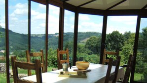 A dining area with a table set for four, surrounded by chairs, under a glass roof with a view of a green landscape.