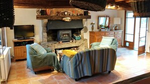 A cozy living room with a stone fireplace, two armchairs, a television, and a wooden cabinet.