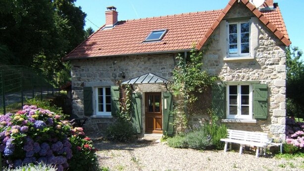 A stone house with a red-tiled roof, a wooden door, and a gravel driveway.