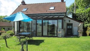 A house with a glass conservatory, a patio with a table and chairs, and a fenced yard.