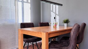 A modern dining area with a wooden table, four chairs, a potted plant, and a bottle of champagne.