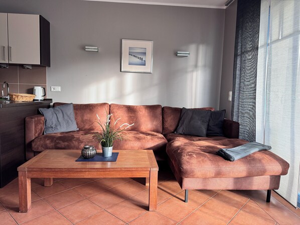 En moderne stue med en lædersofa i brunt, et træbord og en potteplante.