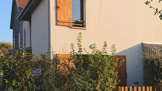 Een tweelaags huis met een schuin dak, een houten deur en een raam met een luik.