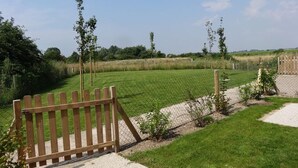 Een houten poort die uitkomt op een grasveld met een omheining en een heldere lucht.