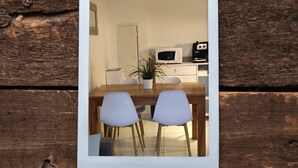 Een eethoek met een houten tafel en twee witte stoelen, een witte magnetron en een koffieapparaat op een wit aanrecht.