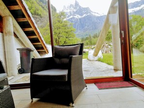 Uma cadeira de vime em um quarto com vista para uma paisagem montanhosa através de grandes portas de vidro.