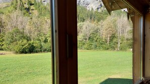 Ein Zimmer mit großem Fenster und Blick auf eine Wiese sowie einen Berg.