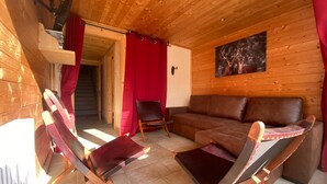 Ein Holzblockhaus-Interieur mit einem braunen Ledersofa, zwei Schaukelstühlen, einem roten Vorhang und einem Bild von einem Reh an der Wand.