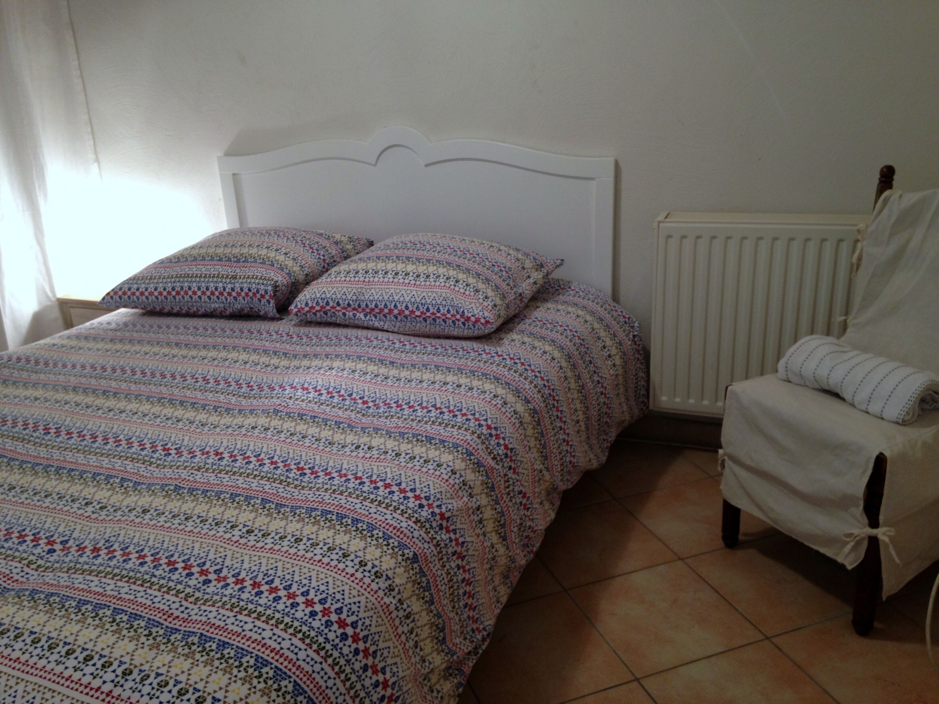 Een slaapkamer met een bed, kussens, een stoel en een radiator.
