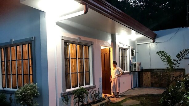 Una casa con porche, una persona de pie en la entrada y un jardín con piedras para caminar.