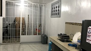 Una cocina con piso de baldosas, un refrigerador, un lavamanos y una ventana con barrotes de metal.