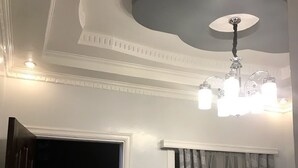 Una habitación con ventilador de techo, sofá de cuero negro, araña y puerta que da al exterior.