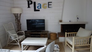 Een woonkamer met een televisie, twee fauteuils, een bank, een open haard en een bordje aan de muur met de tekst 