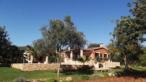 Une villa de style rustique, avec des murs en pierre, un toit en tuiles et un jardin agrémenté de diverses plantes et arbres.