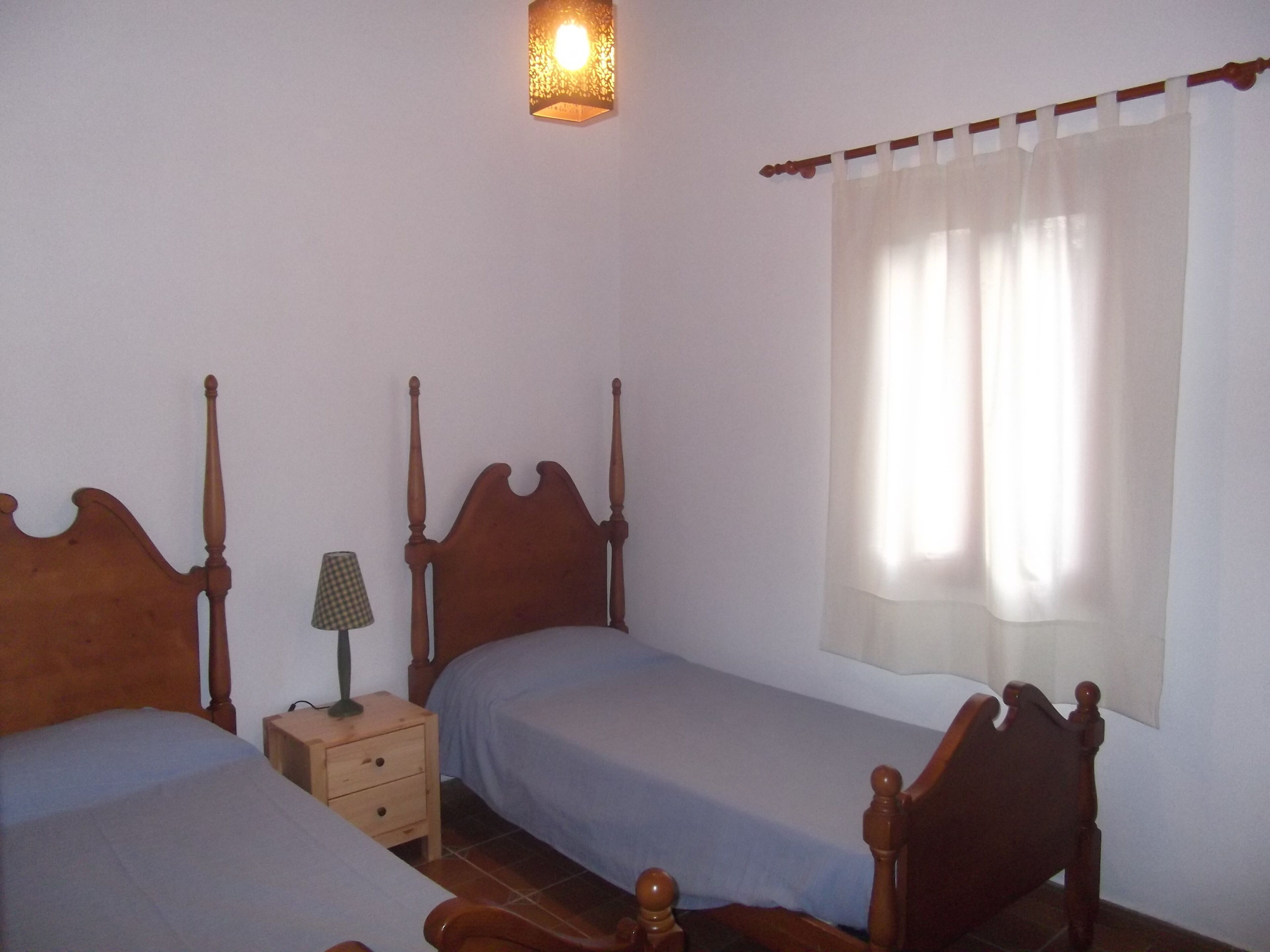 Une chambre à coucher avec deux lits en bois, une table de chevet, une lampe et une fenêtre avec des rideaux.