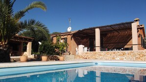 Un espace piscine doté d’une piscine à l’eau cristalline, d’une structure à toit de chaume et d’un mur en pierre.