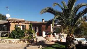 Une maison avec un mur en pierre, un palmier et une piscine.