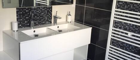 A modern bathroom with a white vanity, a large mirror, and black tiled walls.