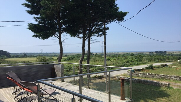 A wooden deck with a metal railing, a pair of lounge chairs, and a view of a rural landscape with trees and a road. - Large house with exceptional sea views in a protected environment (Plouharnel)