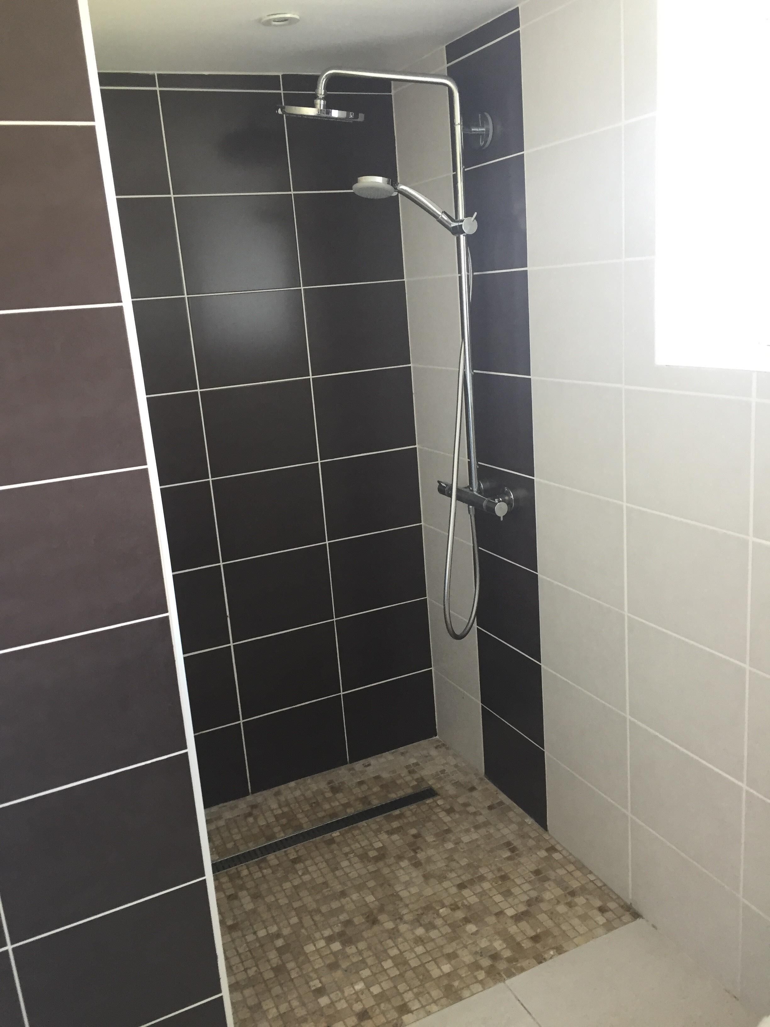 A shower with a handheld showerhead and a wall-mounted faucet, tiled with large black and white tiles.