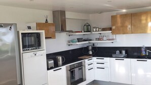 A modern kitchen with white cabinets, stainless steel appliances, and a black countertop. - Large house with exceptional sea views in a protected environment (Plouharnel)