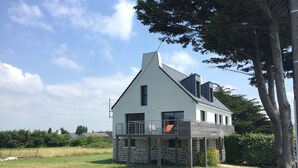 A two-story house with a stone foundation, a balcony with a metal railing, and a clear sky. - Large house with exceptional sea views in a protected environment (Plouharnel)