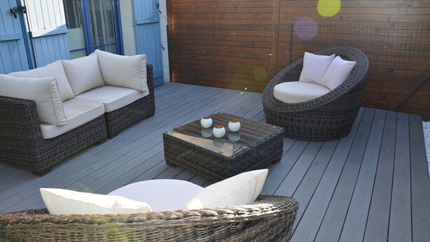 En terrasse med fletmøbler, heriblandt en sofa og en stol, samt et sofabord med glasplade.