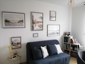 A modern living room with a dark blue sofa, a bookshelf filled with books, and framed landscape paintings on the wall.