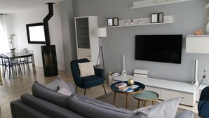 En moderne stue med en grå sofa, en blå lænestol, et spisebord med stole, et fjernsyn ophængt på væggen og en pejs.