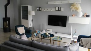 En moderne stue med en grå sofa, en blå lænestol, en sort pejs, et fladskærms-tv og en hvid reol med dekorative genstande.