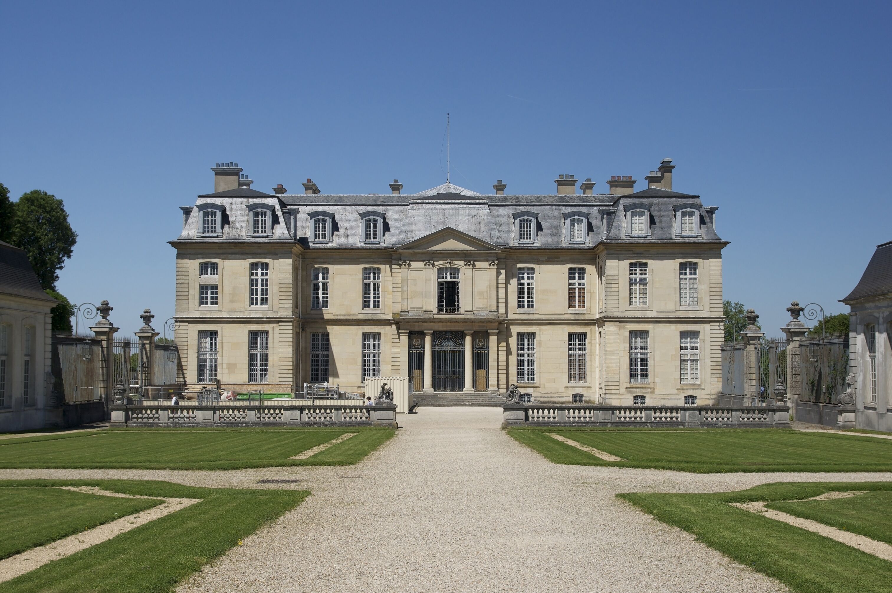 A large, symmetrical building with a central entrance, flanked by manicured lawns and a gravel path leading to the entrance.