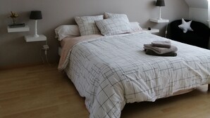 Et soveværelse med en stor seng, en hængende lampe og flere billeder i rammer på væggen.
