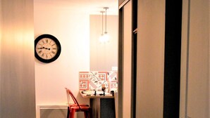 A narrow hallway with a wooden floor leading to a room with a red chair and a wall clock.