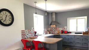 A modern kitchen with a central island, red bar stools, a large clock, and patterned backsplash tiles.