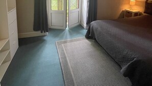 Een slaapkamer met een bed, een nachtkastje, een raam met gordijnen en uitzicht op groen.