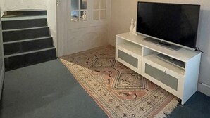 Een kamer met een bed, een televisie op een witte standaard, een kamerkleed met een patroon en een trap.