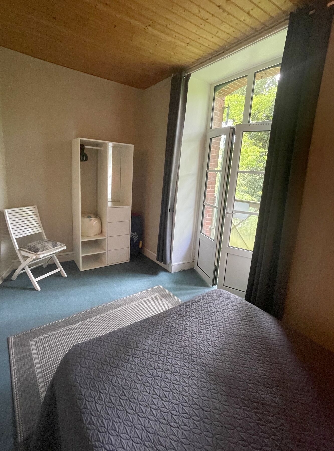 A bedroom with a bed, a chair, a wardrobe, and a window with curtains.